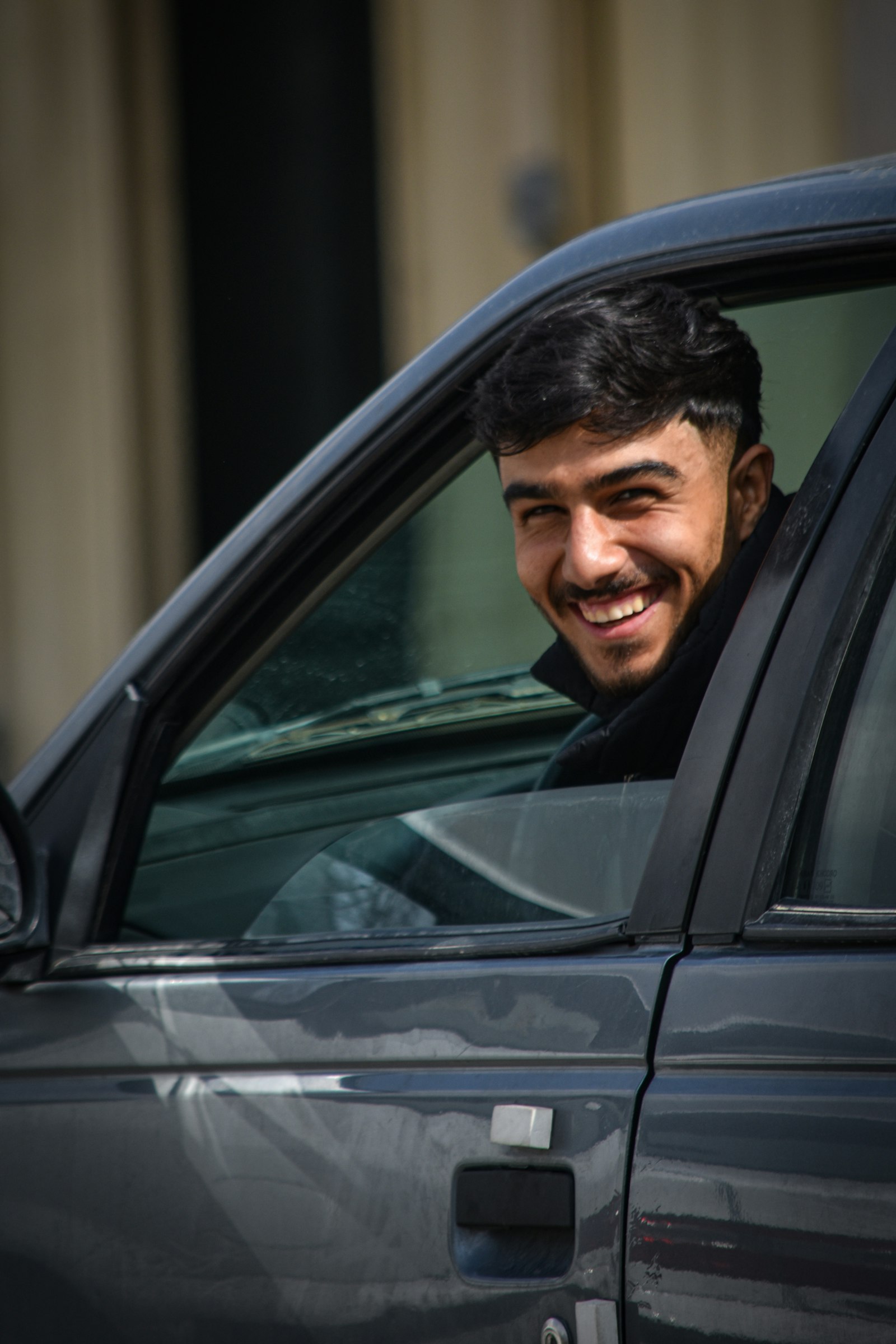 A young driver smiling out of his car window