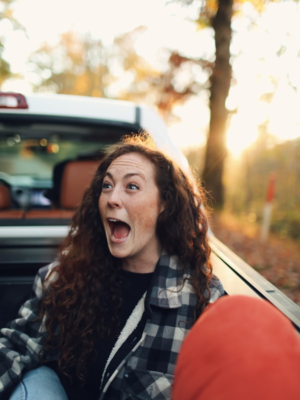 A young woman excited beside her car